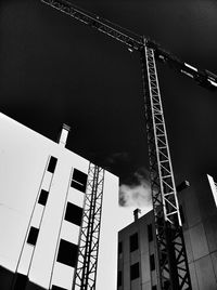 Low angle view of crane by building against sky
