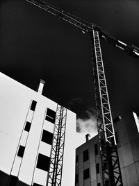 Low angle view of crane by building against sky