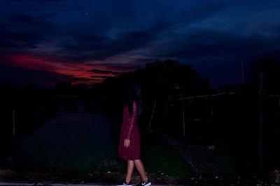 Rear view of woman standing against sky at sunset