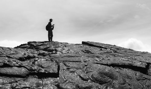 Low angle view of man standing on rock against sky