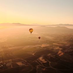 Hot air balloons flying over landscape against sky during sunset