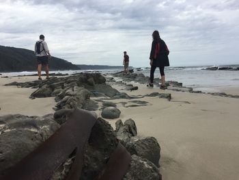 Rear view of people standing on beach against sky