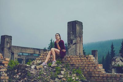 Thoughtful woman sitting on brick wall of abandoned building