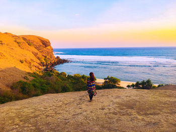 Rear view of woman standing against sea and sky during sunset