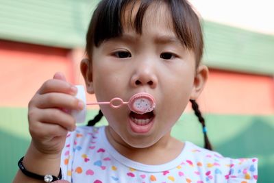 Close-up portrait of cute girl with mouth open holding bubble wand