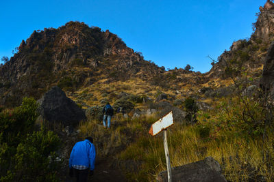 Rear view of people on rock against clear blue sky