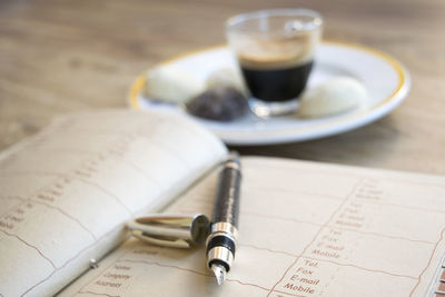 Close-up of pen and book with coffee on table