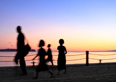 Silhouette people standing on beach against clear sky during sunset