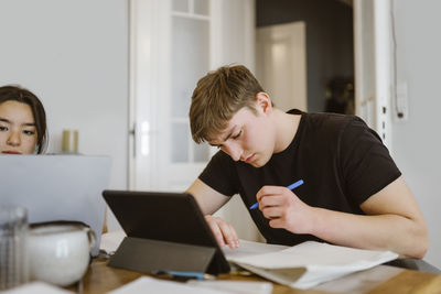 Young man writing while doing homework by friend at home