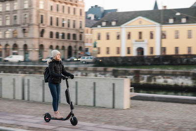 Full length of teenage girl riding e-scooter on street in city