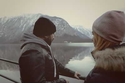 Man and woman wearing knit hat standing by lake during winter