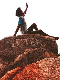 Low angle view of boy on rock against sky