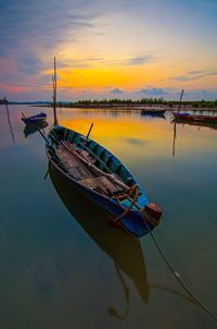 Boat moored in lake against sky during sunset