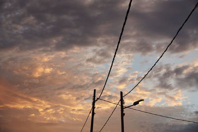 Low angle view of electricity pylon against cloudy sky