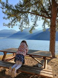 Rear view of woman sitting on railing against sea