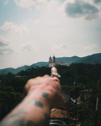 Man holding umbrella by building against sky