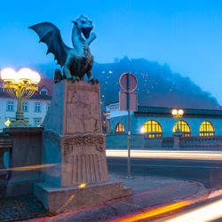 Statue against illuminated city at dusk