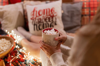 Cup of cocoa or coffee drink with marshmallows in female holding hands of woman in knitted sweater