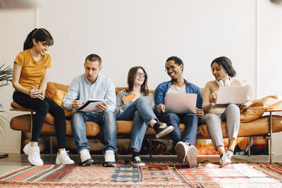 Happy colleagues working together while sitting on sofa in creative office