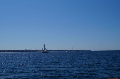 Sailboat sailing in sea against clear blue sky