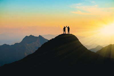 Silhouette people standing on mountain against sky during sunset