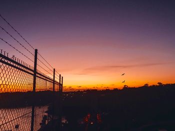 Silhouette fence against orange sky