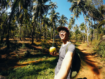 Smiling young man holding coconut water on field during sunny day