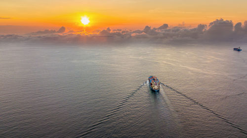 Aerial view of container ship sailing on sea against sky during sunset