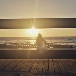 Rear view of woman sitting on beach against sky during sunset