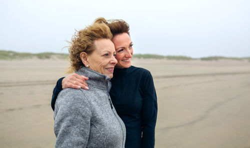 Smiling mother and daughter standing at beach against sky