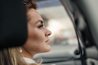 Close-up of young woman looking through window of car 