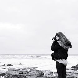 Woman photographing sea against clear sky