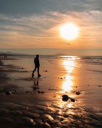 Silhouette woman walking at beach against sky during sunset