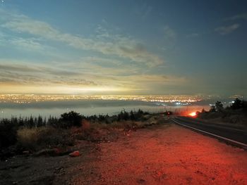 Road amidst illuminated city against sky at sunset