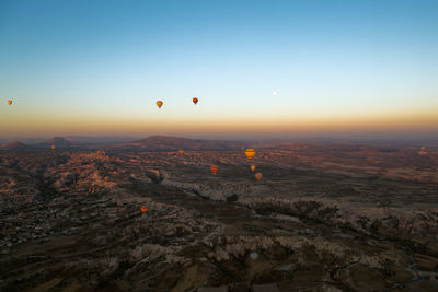 Hot air balloons flying over cappadocia against clear sky during sunset