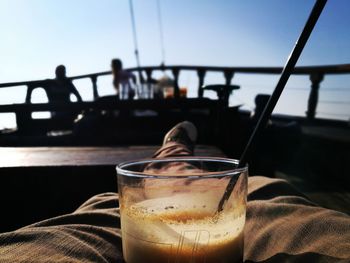 Close-up of hand holding drink by railing against sea