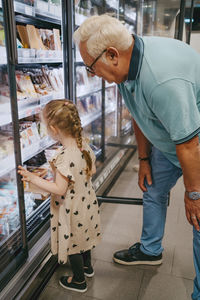 Girl buying frozen foods while doing shopping with grandfather at grocery store