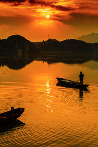 Silhouette man on boat in lake against orange sky