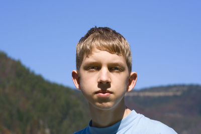 Close-up portrait of boy standing against mountain on sunny day