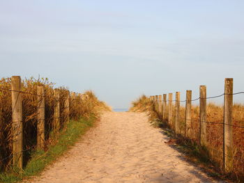 Footpath amidst fence on field against sky