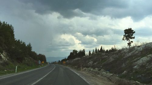 Road by trees against storm clouds