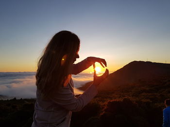 Woman standing against orange sky during sunset