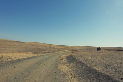 Road amidst desert against clear blue sky