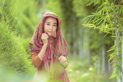 Portrait of young woman standing against trees in park