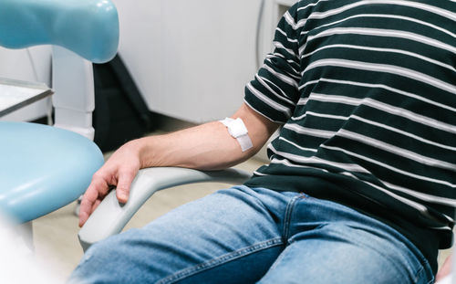 Crop anonymous patient with patch on arm sitting in chair after procedure of blood collection in modern lab