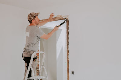 A young caucasian male builder clears a doorway using a crowbar.