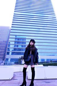 Portrait of young woman standing against modern building