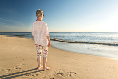 Rear view of woman standing at beach against sky