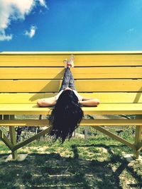 Woman with feet up lying on bench against sky