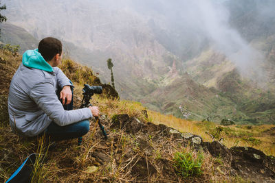 High angle view of man with camera crouching at cliff